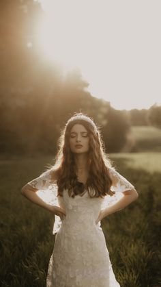 a woman in a white dress standing in the grass with her hands on her hips