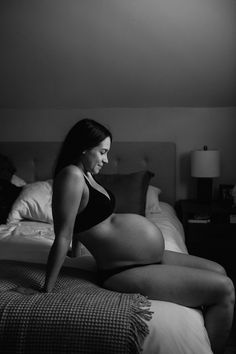 a pregnant woman sitting on top of a bed in a black and white photo,