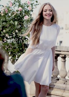 a woman in a white dress is standing on a balcony and smiling at the camera