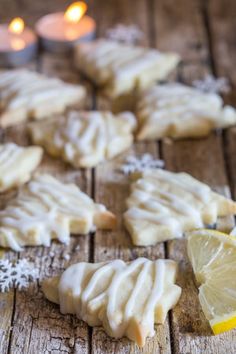 lemon cookies with white icing on a wooden table next to two candles and snowflakes