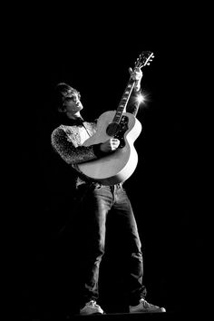 a man holding a guitar while standing in the dark