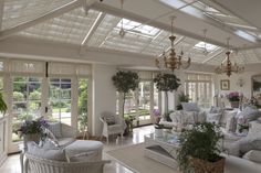 a living room filled with white furniture and lots of plants on top of the tables