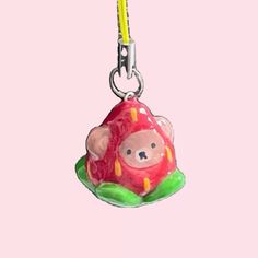 a pink and green animal shaped keychain hanging from a yellow hook on a pink background