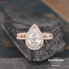 an engagement ring with a pear shaped diamond surrounded by smaller round diamonds on a rock