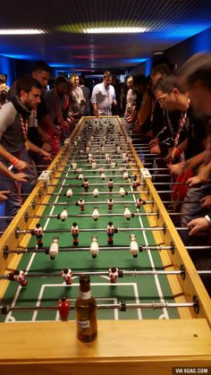 a foo - ball table is lined up with people standing around and looking at it