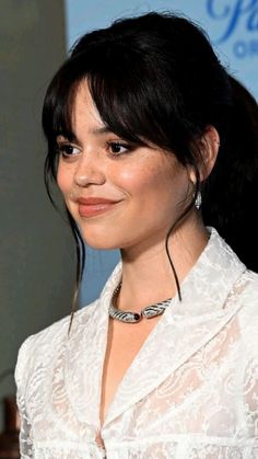 a close up of a person wearing a white shirt and black hair with a smile on her face