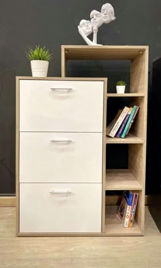 a bookcase with three drawers and a plant on top of it in front of a black wall