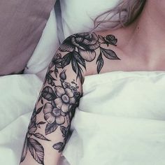 a woman laying in bed with a tattoo on her arm