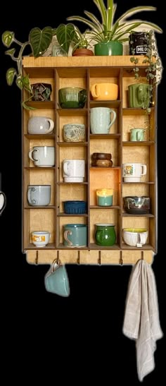 a wooden shelf filled with lots of dishes and cups next to a potted plant