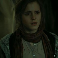 a woman with long hair wearing a scarf and looking at the camera while standing in a dark room