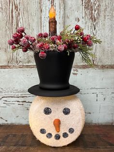 a small snowman with a candle and flowers in it's hat on top of a wooden table