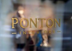 the reflection of two people walking in front of a storefront window that says ponton interiors