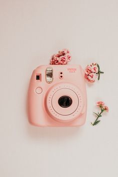 a pink camera sitting on top of a white table next to some flowers and leaves