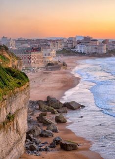 the beach is next to some cliffs and buildings on the other side, as the sun sets