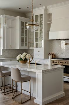 a white kitchen with marble counter tops and gold accents on the cabinets, along with two bar stools