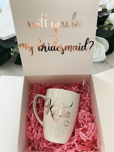 a white coffee mug in a pink box with the words will you be my bridesmaid?