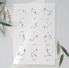 a sheet of paper with zodiac signs and stars on it next to some green leaves