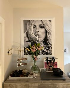 a desk with a laptop and flowers in a vase next to a poster on the wall