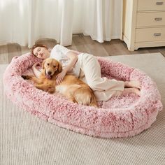 a woman laying in a dog bed on the floor next to a large brown dog