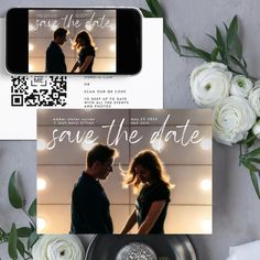 save the date cards with white flowers and greenery are on display in front of a cell phone