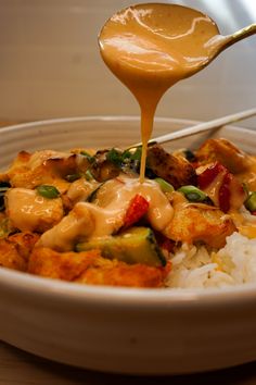 a white bowl filled with rice and vegetables covered in sauce being drizzled over it