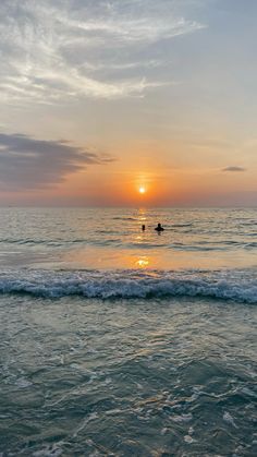 the sun is setting over the ocean with two surfers in the water on their surfboards