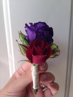 a person is holding a small boutonniere with purple and red flowers on it