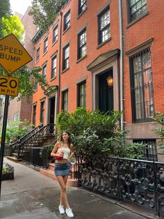 a woman is standing on the sidewalk in front of some brownstone apartment buildings with a speed bump sign