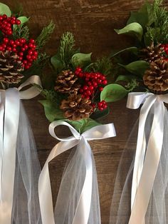 three pine cones with red berries and white ribbon tied around them on a wooden table