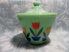 a green ceramic container with flowers painted on the front and sides, sitting on a patterned surface