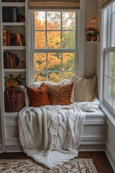 a window seat with pillows and blankets on it in front of a bookshelf