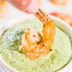 a person dipping shrimp into a bowl of guacamole with a toothpick