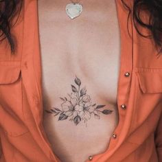 a woman wearing an orange shirt has a flower tattoo on her chest and is looking at the camera