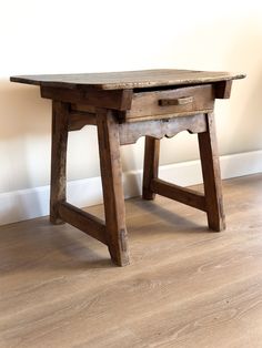 an old wooden table sitting on top of a hard wood floor next to a wall