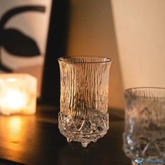 two glass cups sitting on top of a table next to candles and a candle holder