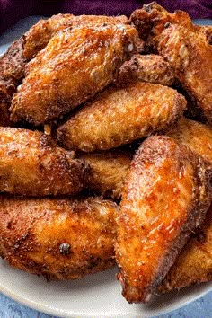 fried chicken wings on a white plate with sugar sprinkled on top and blue cloth in the background