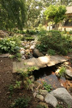 a wooden bridge over a small stream in a garden