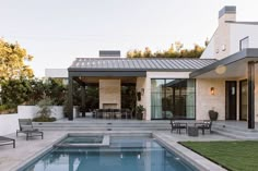 a pool in the middle of a patio with chairs and tables around it, next to a house