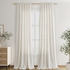 a white curtain hanging on the side of a window next to a potted plant