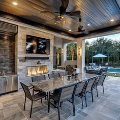 an outdoor kitchen and dining area with fireplace in the center, television on the wall