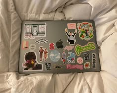 an open laptop computer sitting on top of a bed covered in white sheets and stickers