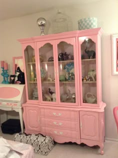 a pink china cabinet with glass doors and drawers in a room filled with toys, decor and other items