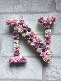 the letter n is made up of flowers on a brick wall and placed in front of a stone wall