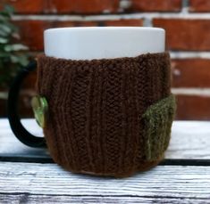 a knitted coffee cup cozys up with a button on the side and is next to a brick wall