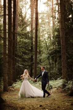 a bride and groom holding hands in the woods