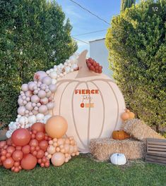 there is a fake pumpkin surrounded by balloons and hay bales on the grass outside