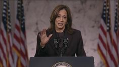 a woman giving a speech in front of american flags