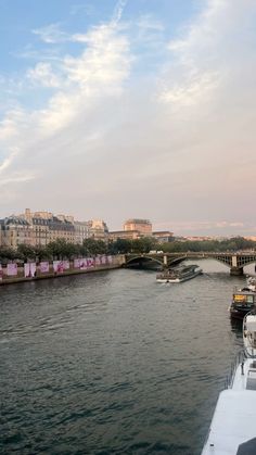 boats on the water in front of a bridge and buildings with pink curtains hanging from them