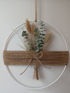 a white circle hanging on a wall with some plants and twine tied to it