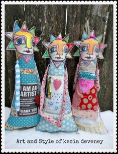 three paper dolls sitting on top of a snow covered ground in front of a wooden fence